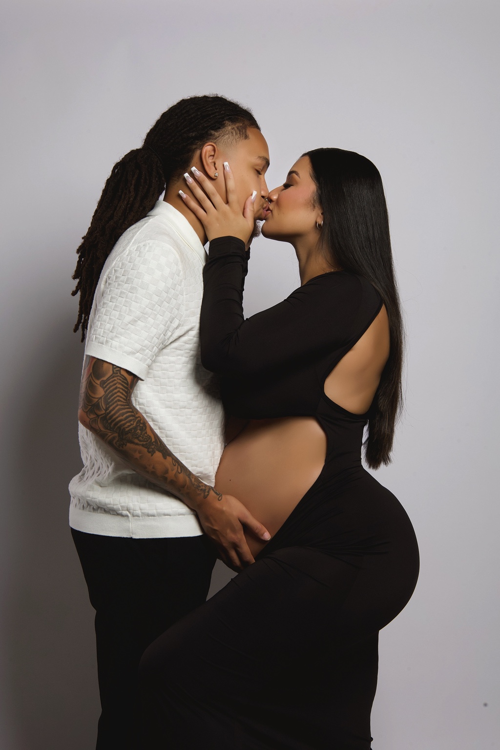 Expecting couple sharing a kiss in black and white looks