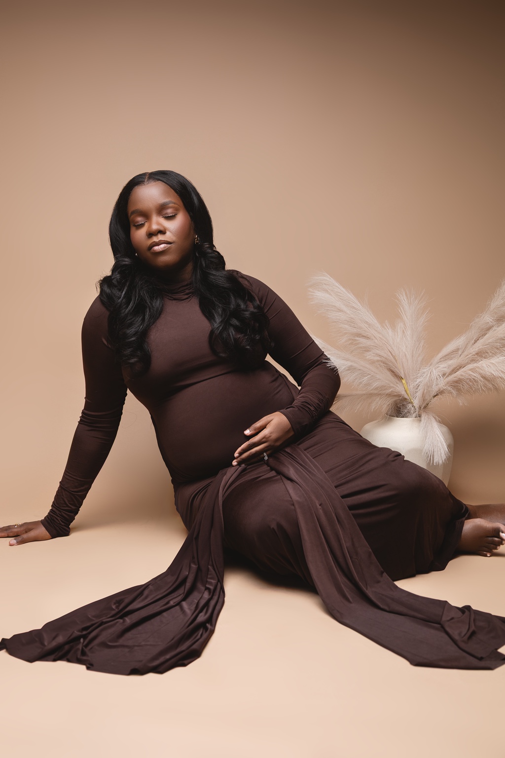 Expecting mother in a flowing brown gown seated in the studio