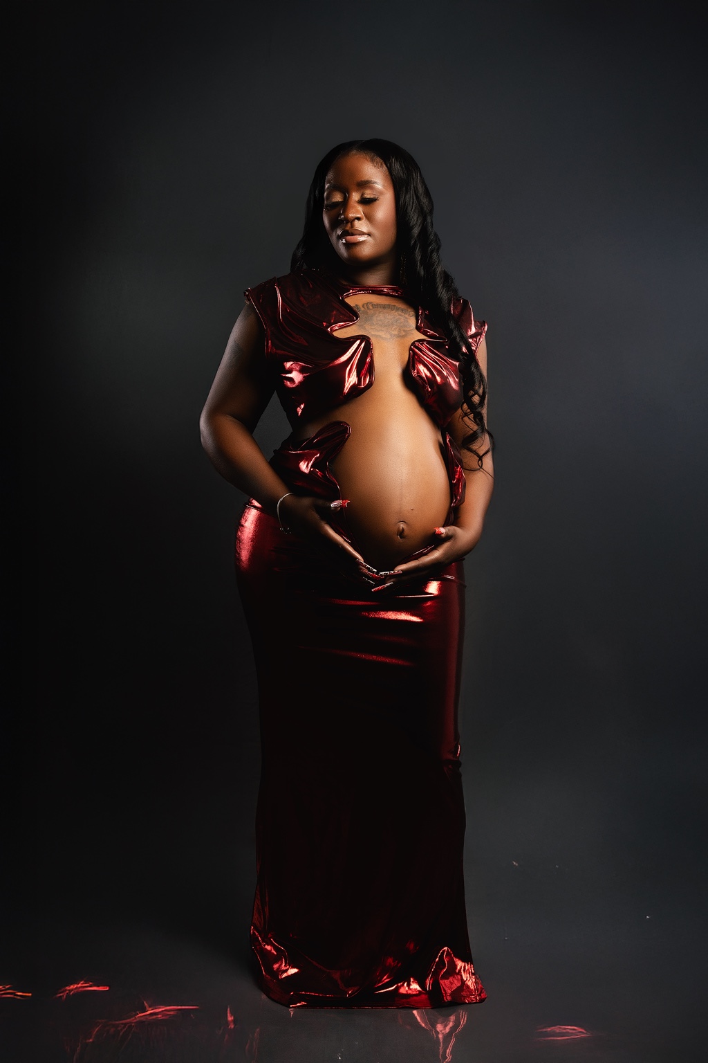 Expecting mother in a red metallic gown with a reflective floor